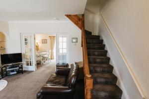 a living room with a staircase with a leather couch at WILLOW COTTAGE - Cost 3 Bed Cottage in Penrhyn Bay with Sea Views with Access to Snowdonia in Llandrillo-yn-Rhôs
