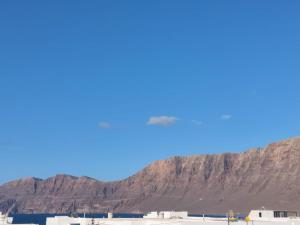 a mountain in front of a blue sky with buildings at Dunas de Famara in Famara
