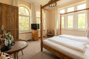 a bedroom with a bed and a table and windows at Hotel Villa Raueneck in Bad Saarow