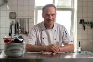 a man in a chefs uniform standing in a kitchen at Hotel Villa Raueneck in Bad Saarow