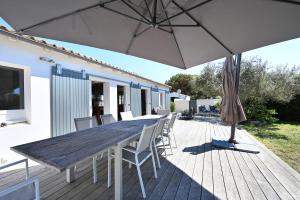 einem Holztisch mit Stühlen und einem Sonnenschirm auf einer Terrasse in der Unterkunft Villa Mer 4 Etoiles - 90 M de la Plage Sea and Mountain Pleasure in Sainte-Marie-de-Ré