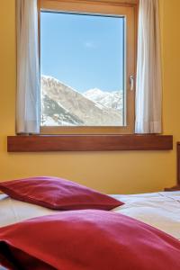 un letto con cuscino rosso di fronte a una finestra di Hotel San Rocco a Livigno