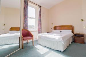 una camera con due letti, una sedia e uno specchio di Falcon's Nest Hotel a Port Erin