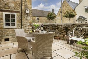 a patio with a table and chairs and a stone wall at Corner Cottage in Adlestrop