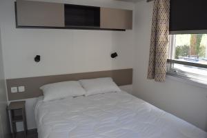een wit bed in een slaapkamer met een raam bij Mobilhome 526 3ch/2SDB camping 4* La Réserve SIBLU Gastes in Gastes