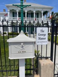 a sign in front of a gate with a white house at The George Manor in Galveston