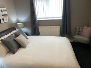a bedroom with a white bed with a chair and a window at Pendle House - Apartment 3 in Colwyn Bay