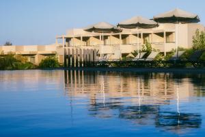 ein Gebäude mit Stühlen und Sonnenschirmen neben einem Wasserkörper in der Unterkunft Giannoulis – Santa Marina Beach Hotel in Agia Marina