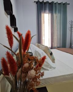un vase rempli de fleurs assis à côté d'un lit dans l'établissement Helena's house, à Ermoúpoli