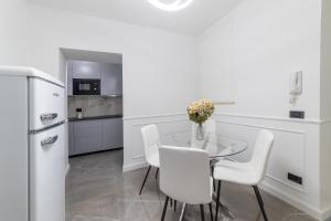 a white kitchen with a glass table and white chairs at iRoome in Rome