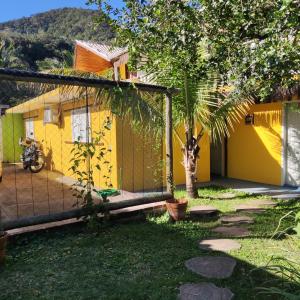 ein gelbes Haus mit einem Zaun und einem Baum in der Unterkunft Céu Azul Casa de Praia in São Sebastião
