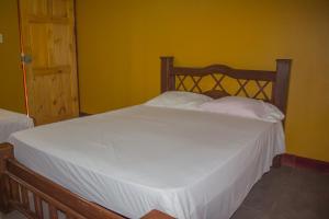 1 dormitorio con cama blanca y pared amarilla en Cabinas Carolina, en Puerto Jiménez