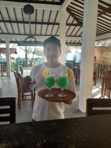 un hombre sosteniendo una bandeja con dos bebidas. en Adinda Bungalows, en Gili Air