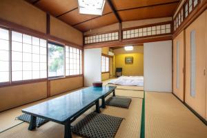 a room with a table and a bed and windows at Daibutsu Ryokan in Takaoka