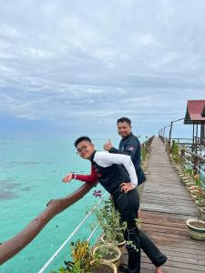 two men sitting on a wooden walkway over the ocean at Pavalintang Resort in Semporna