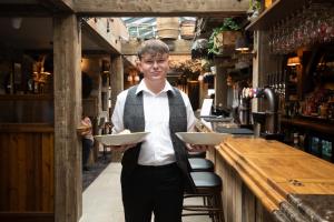 a man holding a plate in front of a bar at The Bamburgh Castle Inn - The Inn Collection Group in Seahouses