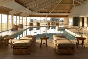 a swimming pool with wicker chairs and tables in a building at Golf View Hotel & Spa in Nairn