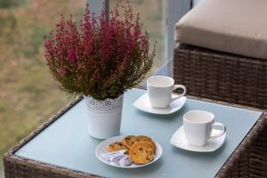 a table with two cups and cookies and a vase with flowers at Apartamenty Jantaris SeaView by Renters in Mielno