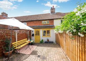 a house with a wooden fence and a bench at Pineapple Cottage in Holt