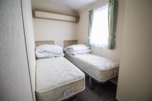 a small room with two beds and a window at Lovely Caravan With Decking At Seawick Holiday Park In Essex Ref 27471sw in Clacton-on-Sea