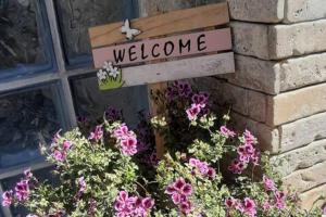 a welcome sign on the side of a building with flowers at Green Rock Villa - gardens, playground and close to beach! in Agios Gordios