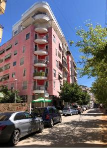 Lovely apartment in the heart of Tirana في تيرانا: مبنى وردي فيه سيارات متوقفة أمامه
