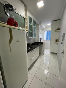 a white kitchen with a refrigerator and a sink at Ap aconchegante 12 min a pé p Praia in Praia Grande