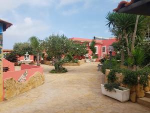 einen Innenhof eines rosa Gebäudes mit Bäumen und Pflanzen in der Unterkunft Residence Villa delle Rose in Lampedusa