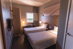 a hotel room with two beds and a television at Ibis Lorena - Circuito da Fé in Lorena