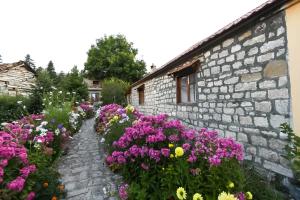 a garden of flowers next to a stone building at Bujtina SHKODRANI in Voskopojë