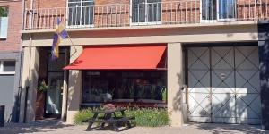 a store front with a red awning and a picnic table in front at Stadsslaperij B&B in Tilburg