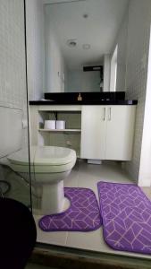 a bathroom with a toilet and two purple rugs at Apartamento Smart Costa Azul in Salvador