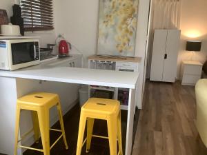 a kitchen with a white counter and two yellow stools at Petite Provence Cottage in Blairgowrie