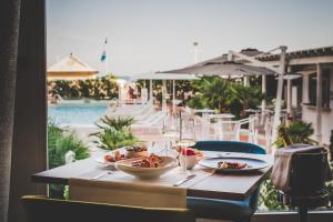 a table with two plates of food and wine and a pool at Hotel Delle Rose in Lido di Jesolo