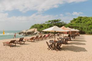 una playa de arena con sillas, mesas y sombrillas en Ecohabs Tequendama Playa Cañaveral Parque Tayrona en El Zaino