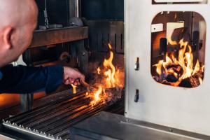 Un uomo che cucina cibo sopra un fuoco in un forno di Hotel Galántha a Eisenstadt