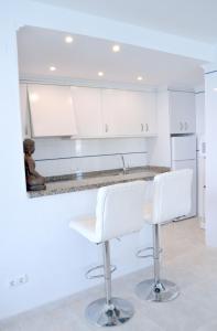 kuchnia z białymi szafkami i białymi stołkami barowymi w obiekcie Firstline apartment RUBINO Arenal-Bol Calpe w mieście Calpe