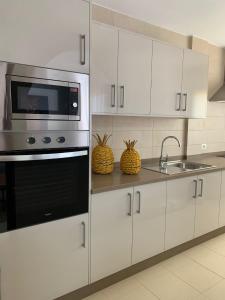 cocina con armarios blancos, microondas y fregadero en Apartamentos Los Catorce, EL Hierro en Valverde