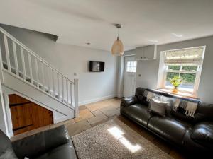a living room with a black leather couch and a staircase at Gorgeous 2-Bed Cottage in Penderyn Brecon Beacons in Aberdare