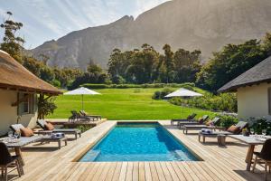 a swimming pool with tables and chairs and a mountain at The Thatch House Hermanus in Hermanus