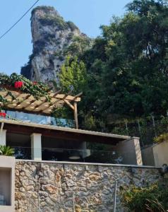 a house with a stone wall with a mountain in the background at Green Rock Villa - gardens, playground and close to beach! in Agios Gordios