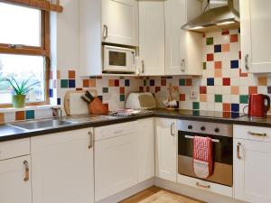 a kitchen with white cabinets and a sink and a microwave at Woodend in Broughton