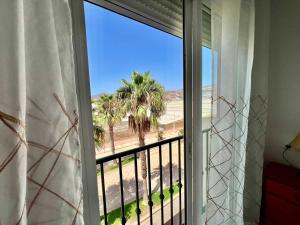 a window with a view of the beach and palm trees at Apartamento Playa Calahonda El Farillo con terraza in Calahonda