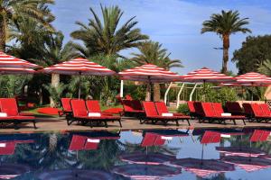 a group of red chairs and umbrellas next to a pool at Mövenpick Hotel Mansour Eddahbi Marrakech in Marrakesh