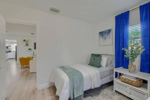 a white bedroom with a bed with blue curtains at Boynton Beach Getaway in Boynton Beach
