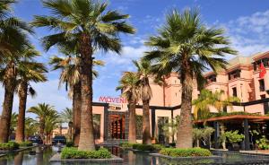a group of palm trees in front of a building at Mövenpick Hotel Mansour Eddahbi Marrakech in Marrakesh