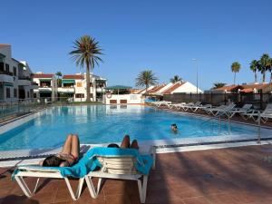 une femme assise sur une chaise à côté d'une piscine dans l'établissement Apartamentos Los Balandros by SunHousesCanarias, à Maspalomas