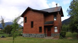 a wooden house with a black roof on a field at Cabañas Peñi Huen in Lago Puelo