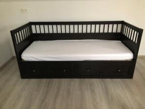 a black bed with white sheets on a wooden floor at Appartement lumineux et calme in Jodoigne