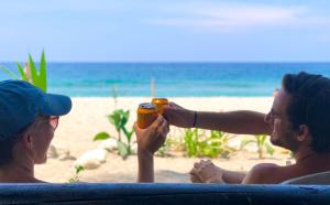 Guachaca的住宿－Hostal Paraíso，两个坐在海滩上喝一杯的男人